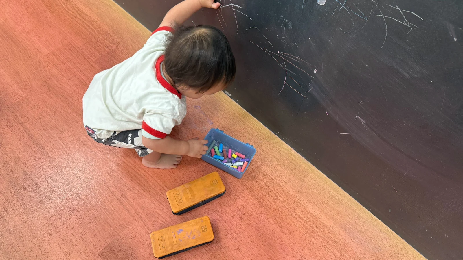 床に座ってチョークで黒板に絵を描く子どもの後ろ姿