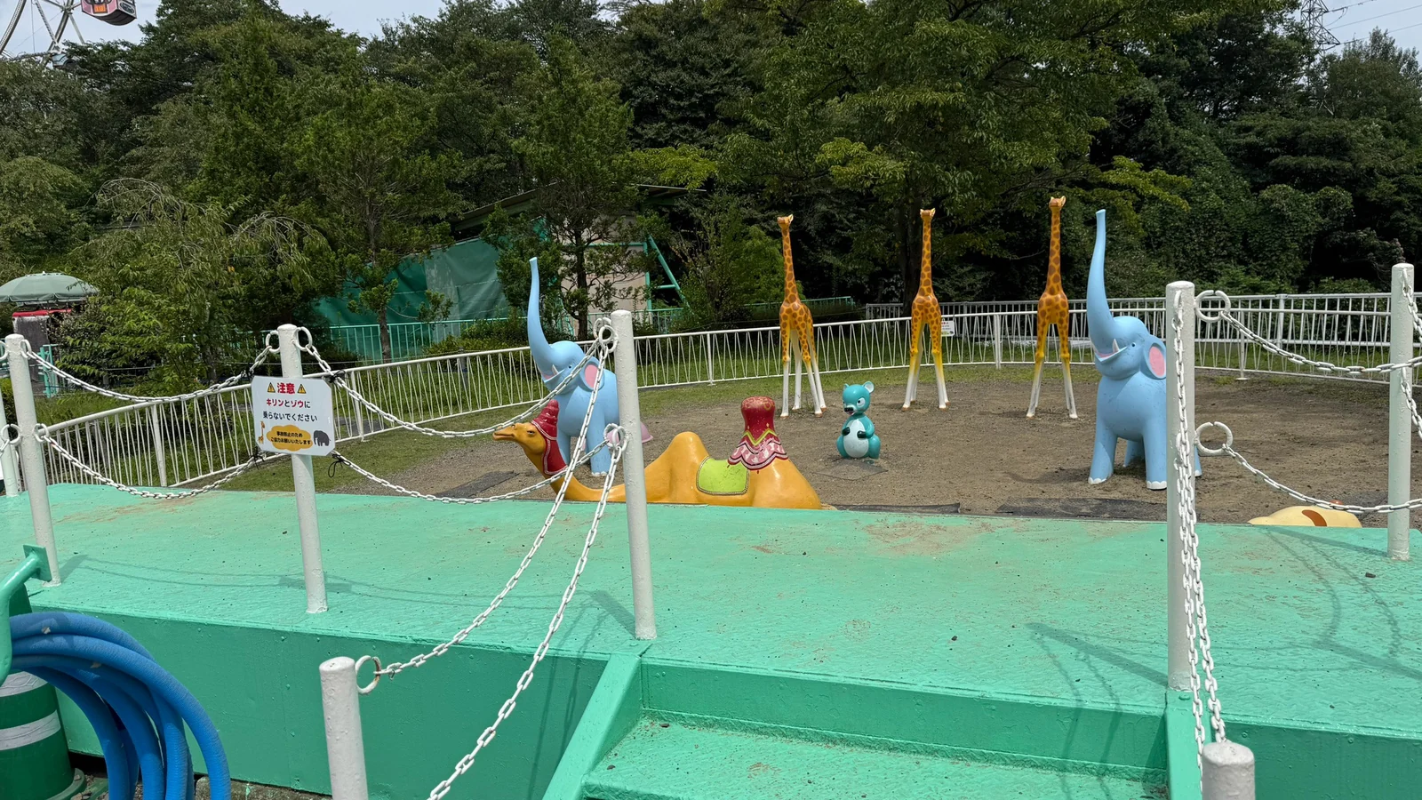 柵に囲まれた緑のデッキと、動物の形のオブジェが並ぶ遊具のエリア