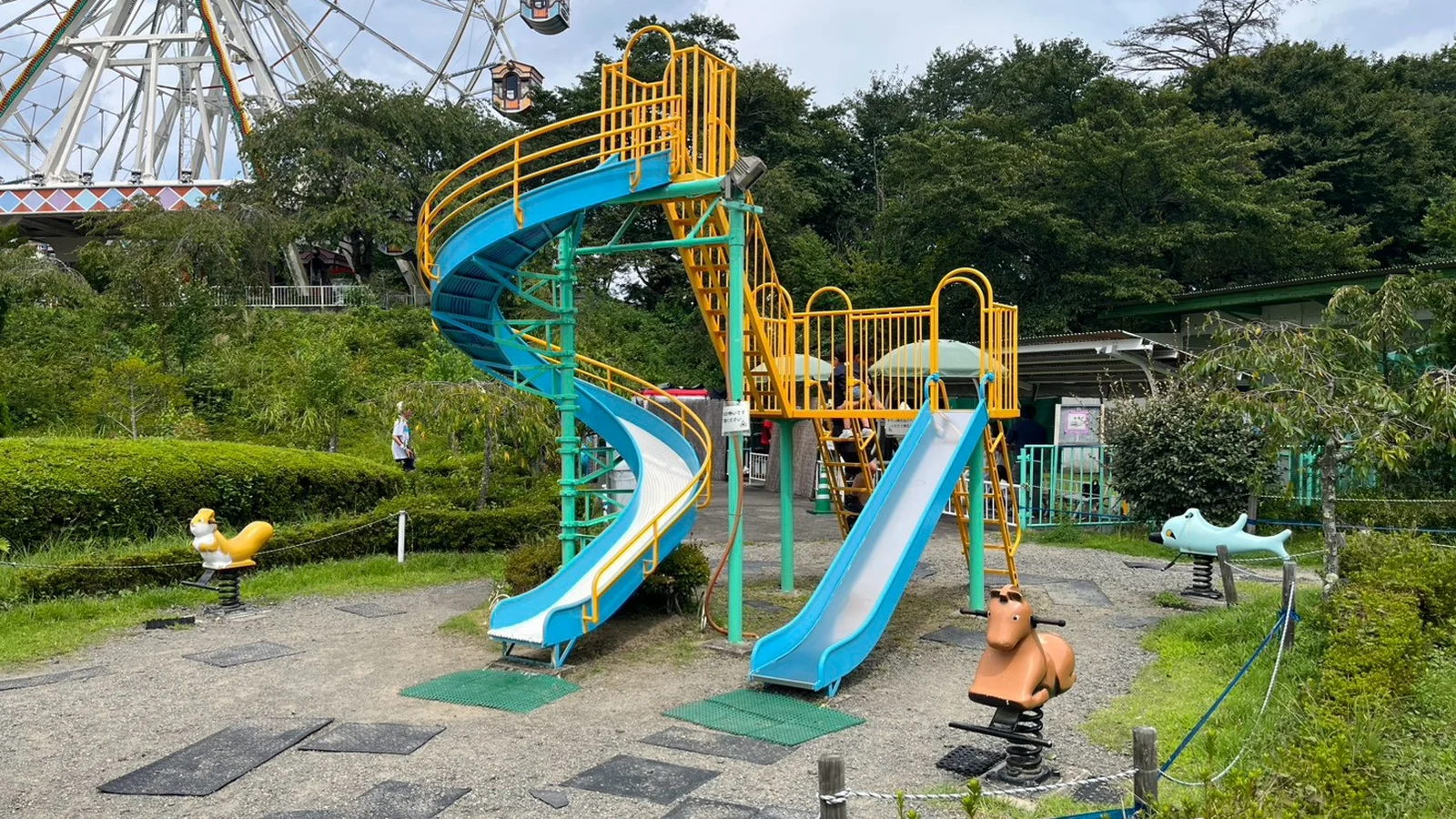 観覧車を背景にした、らせんすべり台付きの複合遊具と揺れる遊具